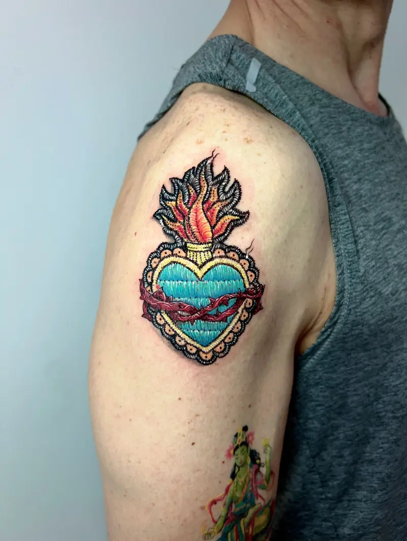 Corazón sagrado estilo parche bordado con llamas y corona de espinas, tonos turquesa y rojos.