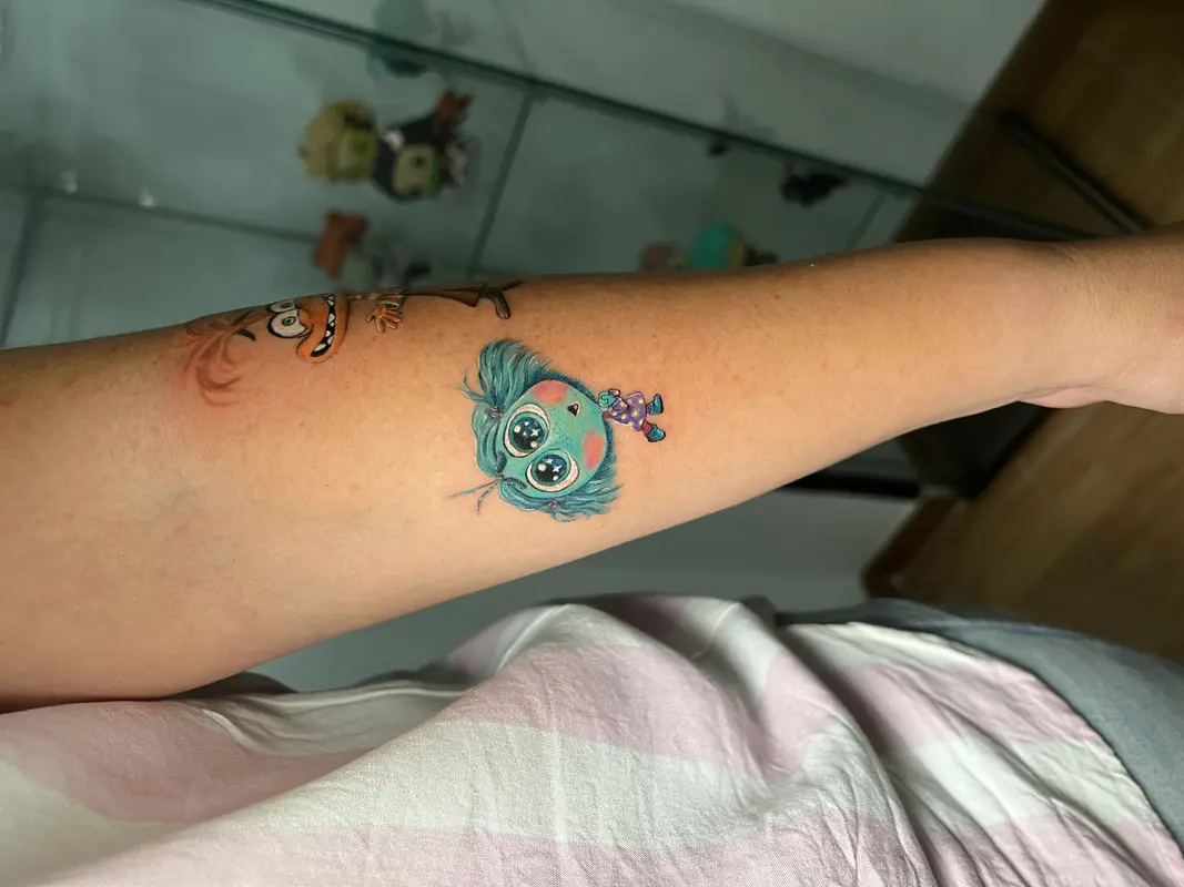 Criatura azul peluda estilo cartoon con ojos enormes, sosteniendo un pequeño muñeco morado.